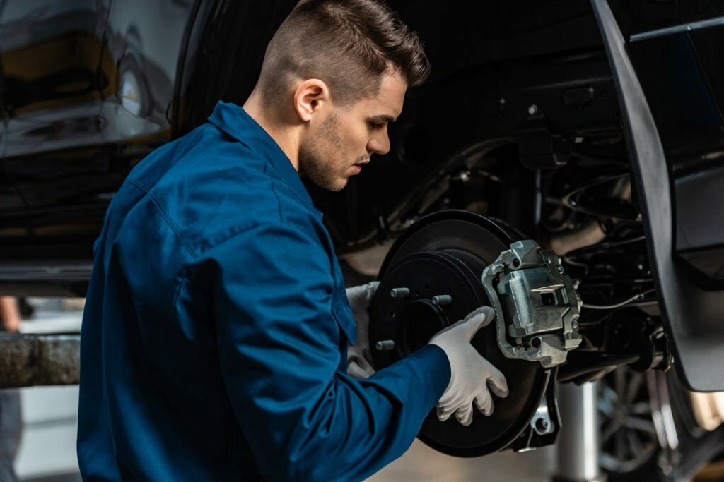 young, attentive mechanic installing disc brakes on raised car